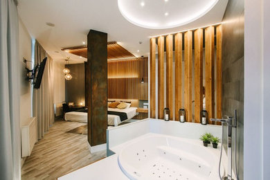 Modelo de cuarto de baño moderno con jacuzzi, ducha a ras de suelo, sanitario de una pieza, paredes grises, suelo de madera en tonos medios, lavabo sobreencimera, suelo blanco y ducha abierta