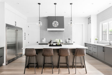 Example of a large transitional u-shaped medium tone wood floor and brown floor open concept kitchen design in Vancouver with an undermount sink, shaker cabinets, gray cabinets, quartz countertops, gray backsplash, stone slab backsplash, stainless steel appliances, an island and gray countertops