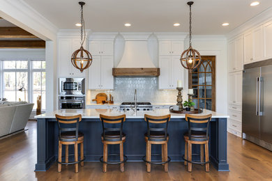 Photo of a large transitional l-shaped open plan kitchen in Raleigh with a farmhouse sink, recessed-panel cabinets, white cabinets, quartz benchtops, blue splashback, stainless steel appliances, medium hardwood floors, with island and white benchtop.