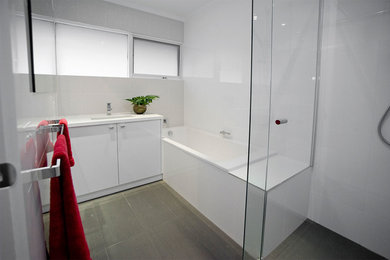 This is an example of a mid-sized modern 3/4 bathroom in Melbourne with flat-panel cabinets, white cabinets, a drop-in tub, an alcove shower, porcelain tile, white walls, ceramic floors, an integrated sink, brown floor and a hinged shower door.