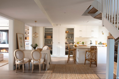 Foto de cocina blanca y madera tradicional renovada de tamaño medio con fregadero bajoencimera, armarios estilo shaker, puertas de armario blancas, encimera de cuarzo compacto, salpicadero blanco, puertas de cuarzo sintético, electrodomésticos negros, suelo de madera en tonos medios, una isla, encimeras blancas y barras de cocina