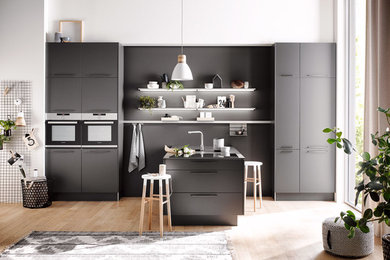 Inspiration for a small modern single-wall eat-in kitchen in Calgary with a single-bowl sink, flat-panel cabinets, grey cabinets, laminate benchtops, grey splashback, timber splashback, black appliances, light hardwood floors, a peninsula, beige floor and grey benchtop.