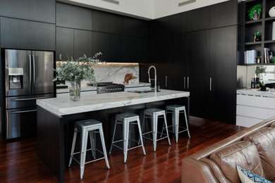 This is an example of a large modern l-shaped open plan kitchen in Brisbane with a double-bowl sink, black cabinets, marble benchtops, white splashback, marble splashback, stainless steel appliances, dark hardwood floors, with island and white benchtop.