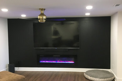 Example of a mid-sized minimalist look-out laminate floor and brown floor basement design in Detroit with black walls and a ribbon fireplace