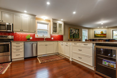 Mid-sized transitional u-shaped medium tone wood floor and brown floor open concept kitchen photo in Ottawa with an undermount sink, flat-panel cabinets, beige cabinets, quartz countertops, red backsplash, stainless steel appliances, a peninsula and multicolored countertops