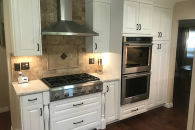 Example of a mid-sized trendy u-shaped dark wood floor enclosed kitchen design in Los Angeles with a farmhouse sink, raised-panel cabinets, white cabinets, quartz countertops, stainless steel appliances and no island
