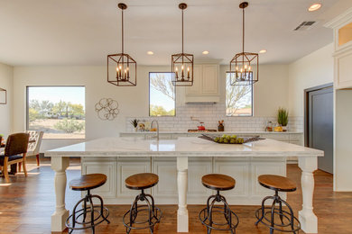 This is an example of a mid-sized transitional l-shaped eat-in kitchen in Phoenix with a farmhouse sink, raised-panel cabinets, white cabinets, marble benchtops, white splashback, subway tile splashback, stainless steel appliances, dark hardwood floors, with island and brown floor.