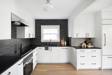 Inspiration for a mid-sized modern l-shaped light wood floor and brown floor enclosed kitchen remodel in Portland with an undermount sink, flat-panel cabinets, white cabinets, granite countertops, black backsplash, ceramic backsplash, black appliances, no island and black countertops