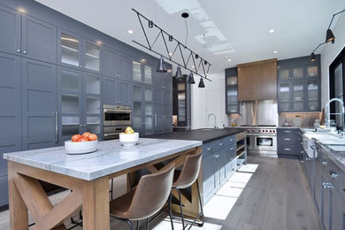 This is an example of an expansive country u-shaped eat-in kitchen in Los Angeles with a farmhouse sink, shaker cabinets, grey cabinets, granite benchtops, white splashback, brick splashback, stainless steel appliances, medium hardwood floors, with island, grey floor and white benchtop.