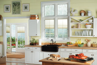 Example of a mid-sized classic single-wall medium tone wood floor and brown floor eat-in kitchen design in Other with a farmhouse sink, raised-panel cabinets, white cabinets, wood countertops, yellow backsplash, wood backsplash, black appliances and an island