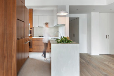Inspiration for a small contemporary l-shaped porcelain tile and beige floor open concept kitchen remodel in New York with an undermount sink, flat-panel cabinets, medium tone wood cabinets, solid surface countertops, stainless steel appliances, a peninsula, white backsplash and white countertops