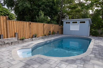 This is an example of a modern backyard custom-shaped pool in Toronto with brick pavers.