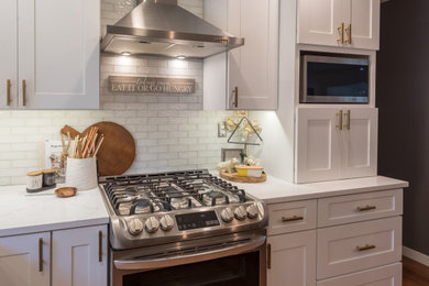 Inredning av ett klassiskt litet vit vitt kök, med en undermonterad diskho, skåp i shakerstil, vita skåp, bänkskiva i kvartsit, vitt stänkskydd, stänkskydd i tunnelbanekakel, rostfria vitvaror, mörkt trägolv, en köksö och brunt golv