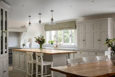 This is an example of a farmhouse u-shaped kitchen/diner in Other with recessed-panel cabinets, beige cabinets, quartz worktops, stainless steel appliances, slate flooring, an island, beige worktops and a chimney breast.