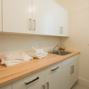 Design ideas for a small modern single-wall utility room in Calgary with a built-in sink, flat-panel cabinets, white cabinets, wood worktops and plywood flooring.