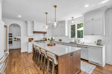 Example of a large arts and crafts l-shaped medium tone wood floor and brown floor kitchen pantry design in Indianapolis with an undermount sink, recessed-panel cabinets, white cabinets, quartzite countertops, white backsplash, porcelain backsplash, white appliances, an island and white countertops