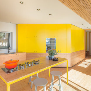 Свежая идея для дизайна: большая угловая кухня в современном стиле с обеденным столом, одинарной раковиной, плоскими фасадами, желтыми фасадами, деревянной столешницей, техникой под мебельный фасад, светлым паркетным полом, островом, бежевым полом и бежевой столешницей - отличное фото интерьера