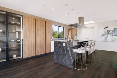 Inspiration for a mid-sized modern galley medium tone wood floor and brown floor kitchen remodel in Los Angeles with flat-panel cabinets, white cabinets, stainless steel countertops, black appliances, an island and gray countertops