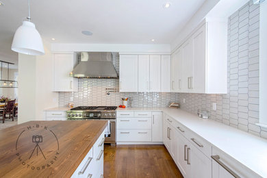 Large single-wall medium tone wood floor and brown floor open concept kitchen photo with recessed-panel cabinets, white cabinets, wood countertops, white backsplash, ceramic backsplash, stainless steel appliances, an island and brown countertops
