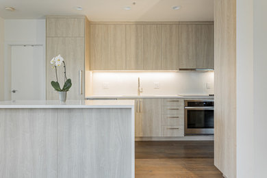 Eat-in kitchen - mid-sized modern l-shaped medium tone wood floor and coffered ceiling eat-in kitchen idea in Vancouver with a double-bowl sink, flat-panel cabinets, light wood cabinets, quartz countertops, white backsplash, quartz backsplash, paneled appliances, an island and white countertops