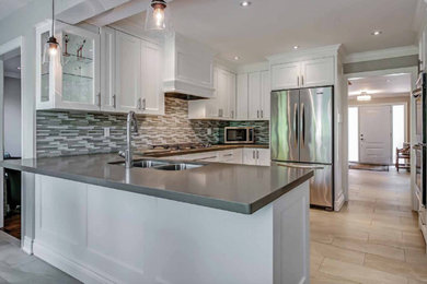Mid-sized transitional u-shaped eat-in kitchen in Toronto with a double-bowl sink, shaker cabinets, white cabinets, quartz benchtops, grey splashback, glass sheet splashback, stainless steel appliances and ceramic floors.