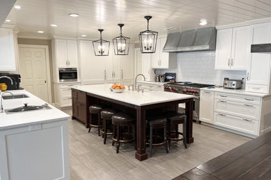 Inspiration for an expansive modern galley open plan kitchen in New York with a farmhouse sink, raised-panel cabinets, white cabinets, quartz benchtops, white splashback, ceramic splashback, stainless steel appliances, porcelain floors, with island, grey floor, white benchtop and wood.