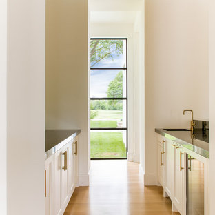 Foto de bar en casa con fregadero de galera, mediterráneo, de tamaño medio, con fregadero bajoencimera, armarios con paneles empotrados, puertas de armario blancas, encimera de mármol, suelo de madera clara y encimeras negras