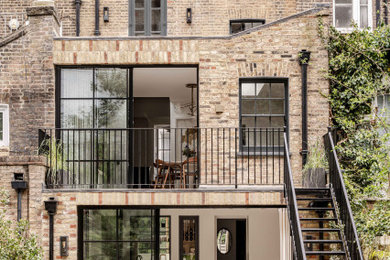 Photo of a large and brown contemporary brick and rear house exterior in London with four floors, a black roof, a mansard roof and a tiled roof.