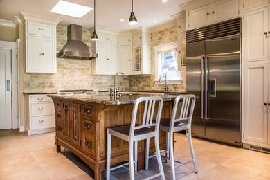 Example of a large transitional l-shaped travertine floor and beige floor enclosed kitchen design in San Francisco with an undermount sink, shaker cabinets, white cabinets, granite countertops, beige backsplash, stone tile backsplash, stainless steel appliances and an island