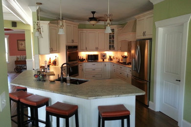 Inspiration for a large timeless l-shaped medium tone wood floor open concept kitchen remodel in Charlotte with a farmhouse sink, glass-front cabinets, beige cabinets, granite countertops, multicolored backsplash, stone tile backsplash and stainless steel appliances