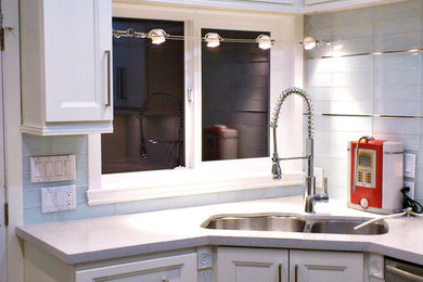 Small elegant kitchen photo in Vancouver with a double-bowl sink, glass-front cabinets, white cabinets, quartz countertops, white backsplash, glass tile backsplash, stainless steel appliances and a peninsula
