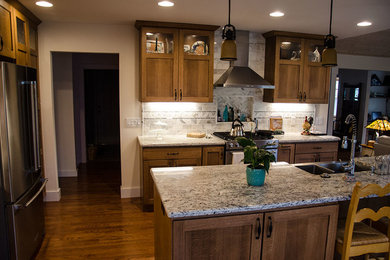 Example of a large arts and crafts l-shaped medium tone wood floor and brown floor open concept kitchen design in New York with recessed-panel cabinets, dark wood cabinets, white backsplash, cement tile backsplash, stainless steel appliances, an island, a farmhouse sink and granite countertops