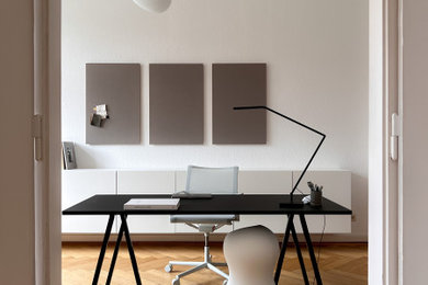 Mittelgroßes Modernes Arbeitszimmer mit weißer Wandfarbe, braunem Holzboden, freistehendem Schreibtisch und braunem Boden in Leipzig