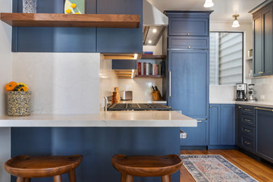 Inspiration for a large midcentury u-shaped eat-in kitchen in San Francisco with a farmhouse sink, recessed-panel cabinets, blue cabinets, marble benchtops, white splashback, marble splashback, stainless steel appliances, medium hardwood floors and white benchtop.