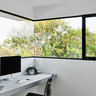 This is an example of a medium sized modern home studio in Geelong with white walls, light hardwood flooring, a built-in desk and brown floors.