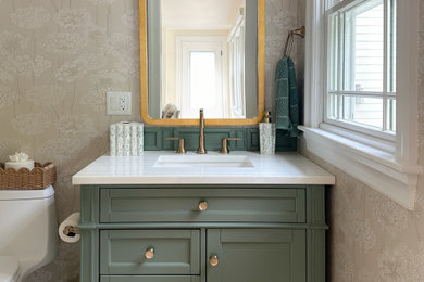 Inspiration for a farmhouse beige floor and wallpaper powder room remodel in Boston with recessed-panel cabinets, green cabinets, beige walls, an undermount sink, white countertops and a freestanding vanity