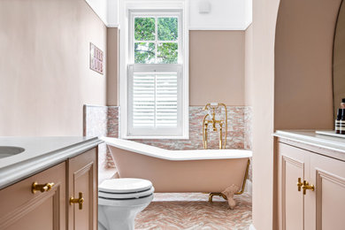 Photo of a traditional bathroom in Hertfordshire with recessed-panel cabinets, a claw-foot bath, pink tiles, pink walls, a submerged sink, pink floors, white worktops and a built in vanity unit.