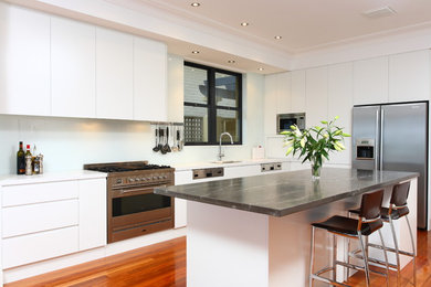 Large modern eat-in kitchen in Central Coast with an undermount sink, flat-panel cabinets, white cabinets, marble benchtops, white splashback, glass sheet splashback, stainless steel appliances, medium hardwood floors and with island.