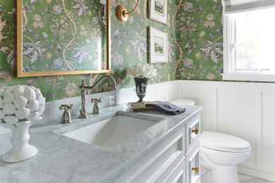 Inspiration for a timeless marble floor and wallpaper powder room remodel in New York with furniture-like cabinets, white cabinets, a one-piece toilet, an undermount sink, marble countertops and a built-in vanity