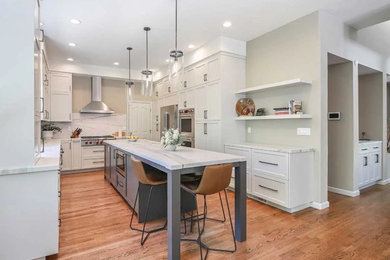 Example of a large transitional galley medium tone wood floor and brown floor open concept kitchen design in San Francisco with an undermount sink, shaker cabinets, white cabinets, solid surface countertops, multicolored backsplash, stainless steel appliances, an island and multicolored countertops