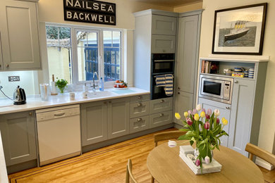 Inspiration for a medium sized traditional u-shaped kitchen/diner in Other with shaker cabinets, blue cabinets, composite countertops, white splashback, black appliances, no island, white worktops, an integrated sink and light hardwood flooring.