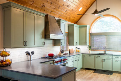 Inspiration for a transitional u-shaped light wood floor, brown floor and vaulted ceiling kitchen pantry remodel in Boston with an undermount sink, shaker cabinets, green cabinets, granite countertops, white backsplash, stainless steel appliances, black countertops and ceramic backsplash