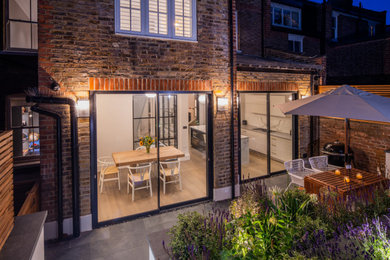 Photo of a small modern back patio in London with a bbq area, natural stone paving and a pergola.