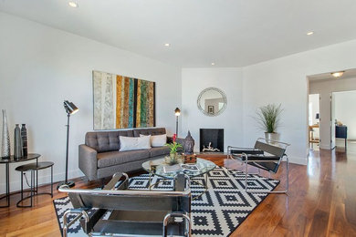 This is an example of a mid-sized modern enclosed living room in San Francisco with white walls, dark hardwood floors, a corner fireplace, a wood fireplace surround, no tv and brown floor.