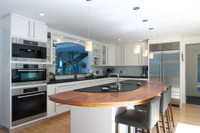 Inspiration for a mid-sized mid-century modern l-shaped light wood floor eat-in kitchen remodel in Portland Maine with an undermount sink, flat-panel cabinets, white cabinets, wood countertops, white backsplash, stainless steel appliances and an island