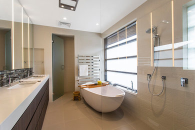 This is an example of a mid-sized contemporary master bathroom in Melbourne with beige tile, porcelain tile, dark wood cabinets, a freestanding tub, a double shower, a wall-mount toilet, beige walls, an undermount sink, furniture-like cabinets and engineered quartz benchtops.