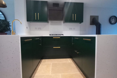 This is an example of a contemporary u-shaped open plan kitchen in Gloucestershire with a built-in sink, flat-panel cabinets, green cabinets, composite countertops, beige splashback, integrated appliances, limestone flooring, beige worktops and feature lighting.