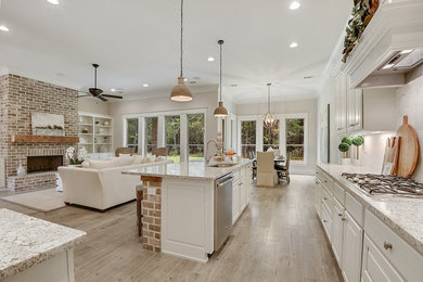 Mid-sized transitional l-shaped open plan kitchen in New Orleans with an undermount sink, raised-panel cabinets, white cabinets, granite benchtops, grey splashback, stone tile splashback, stainless steel appliances, light hardwood floors, with island and beige floor.