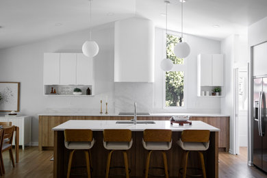 Inspiration for a modern medium tone wood floor, brown floor and vaulted ceiling kitchen remodel in Raleigh with an undermount sink, quartz countertops, white backsplash, quartz backsplash, stainless steel appliances, an island and white countertops