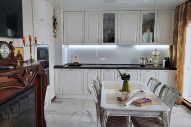 This is an example of a mid-sized transitional single-wall eat-in kitchen in Saint Petersburg with a single-bowl sink, raised-panel cabinets, white cabinets, quartz benchtops, white splashback, glass sheet splashback, black appliances, no island and brown benchtop.